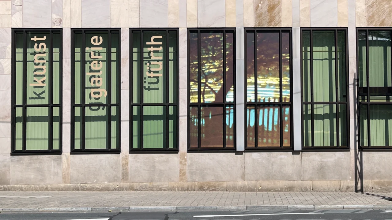 Fassade der Kunstgalerie mit großen Fenstern, in denen die Wörter 'kunst galerie fürth' vertikal angeordnet sind. In zwei Fenstern ist eine Fotografie zu sehen.