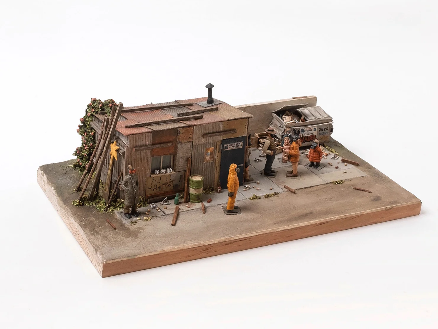 Miniaturszene mit einem kleinen, verwitterten Holzhaus, mehreren Figuren in Winterkleidung und einem alten Auto auf einem rechteckigen Sockel.