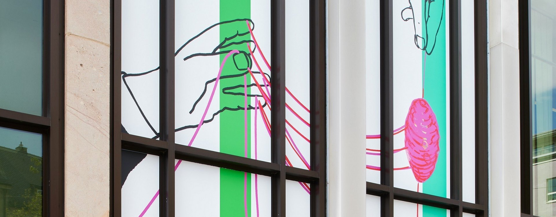 Fensterfront der Kunstgalerie mit moderner Kunst, die Hände zeigt, die pinken Faden halten, vor weißem Hintergrund mit grünen senkrechten Streifen